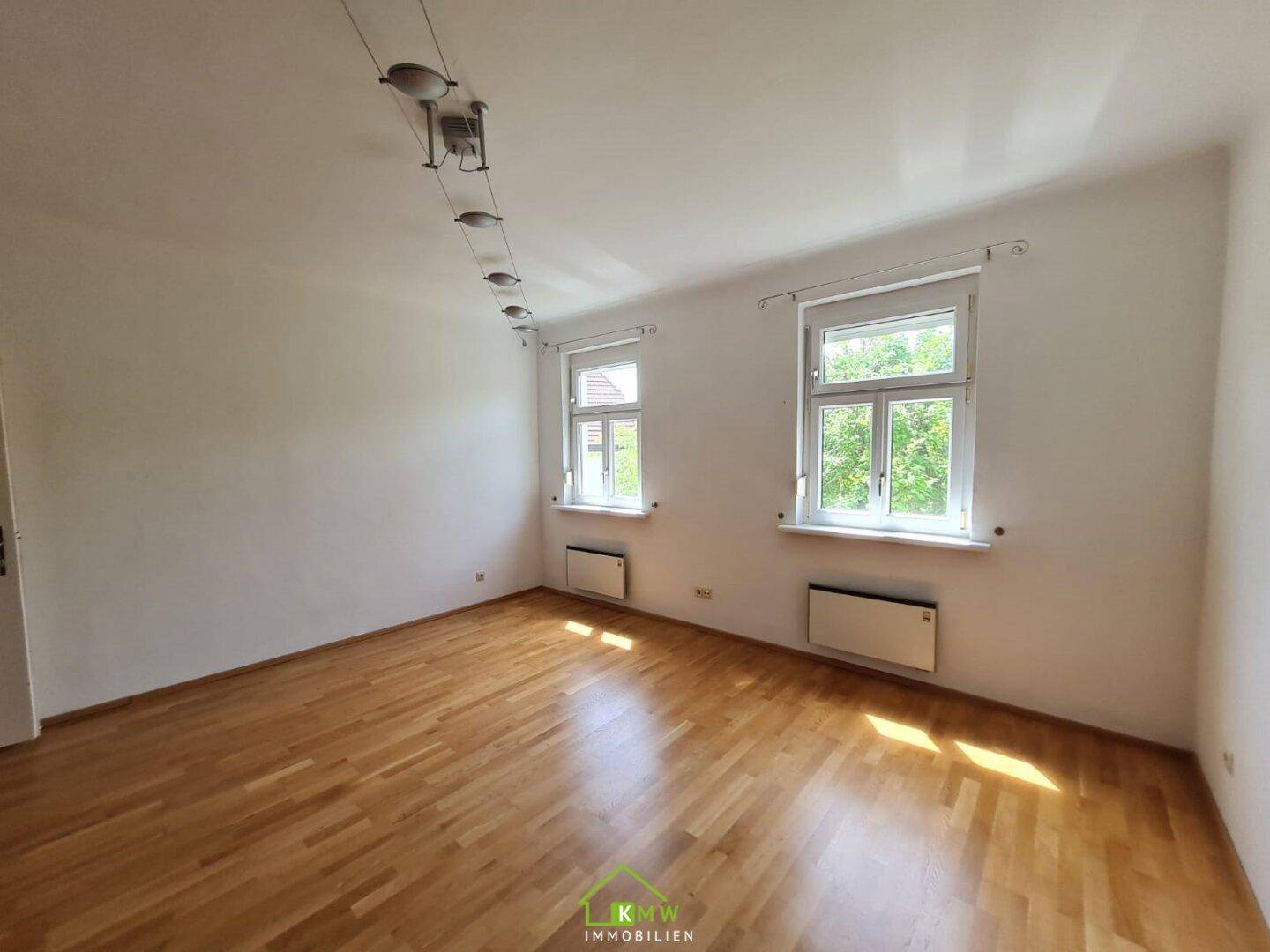 Helles Wohnzimmer mit zwei Fenstern und warmem Holzfußboden, bereit zur individuellen Gestaltung.
