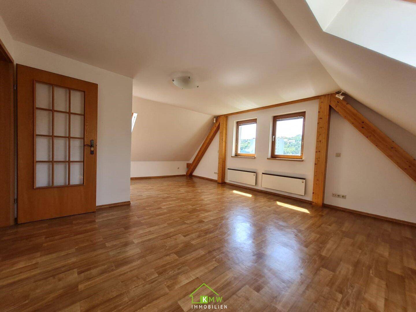 Helles Dachzimmer mit Holzfußboden, sichtbaren Balken und Fenstern, die viel Licht spenden.