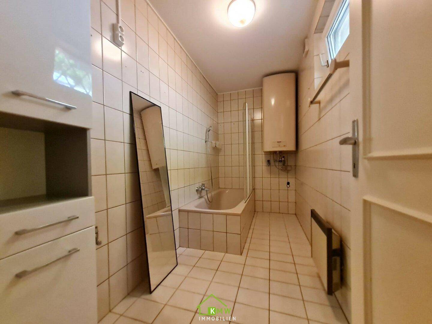 Gefliestes Badezimmer mit Badewanne und Duschfunktion sowie einem Fenster für Tageslicht.