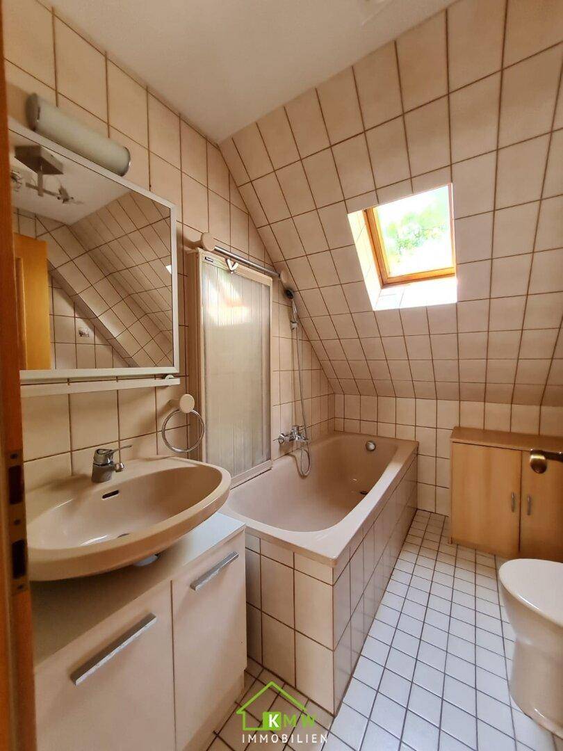 Gefliestes Badezimmer im Dachgeschoss mit Badewanne, Waschbecken und Dachfenster.