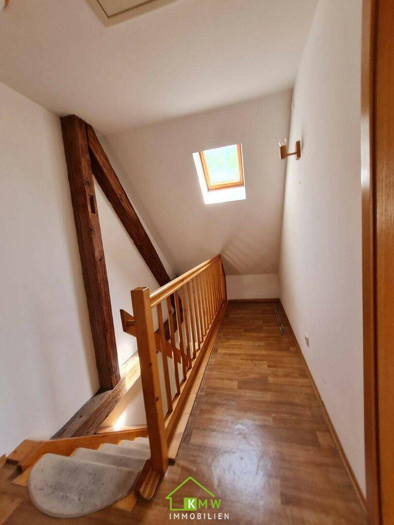 Treppenaufgang zum Dachgeschoss mit Holzgeländer, sichtbaren Balken und Dachfenster.