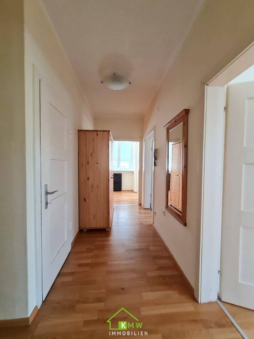 Langer Flur mit Holzparkett und einem Holzschrank, der zu weiteren Räumen führt.