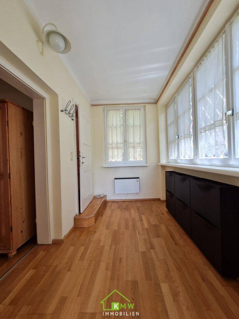 Heller Eingangsbereich mit Holzfußboden und Fenstern, die viel Tageslicht hereinlassen.