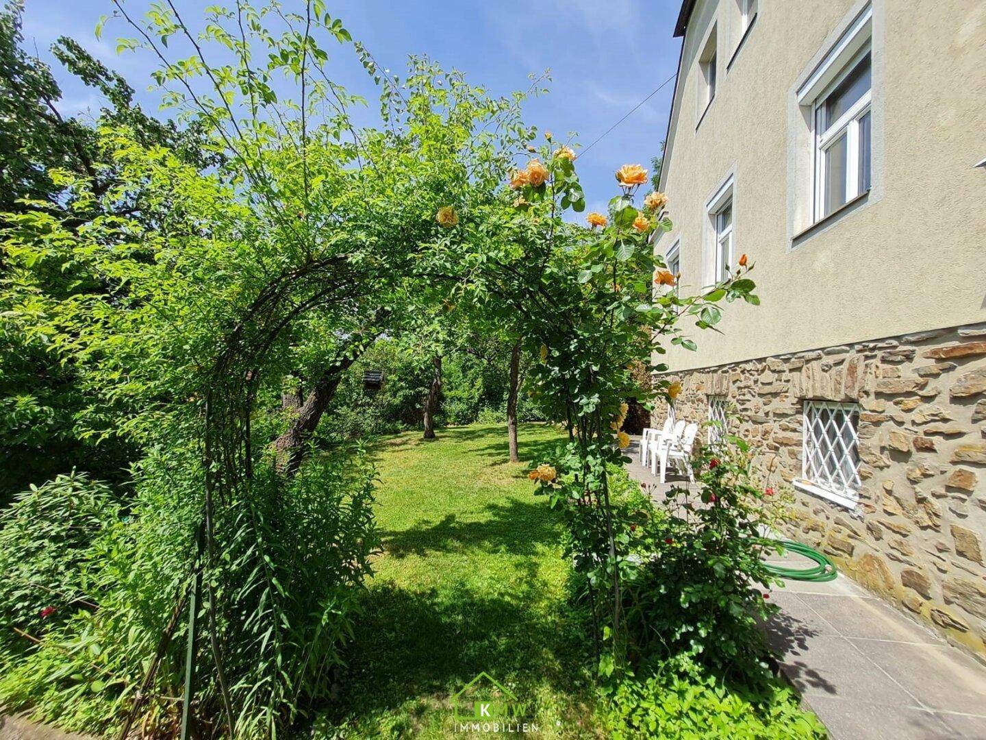 Romantischer Gartenbereich mit Rosenbogen und kleiner Terrasse am Haus.