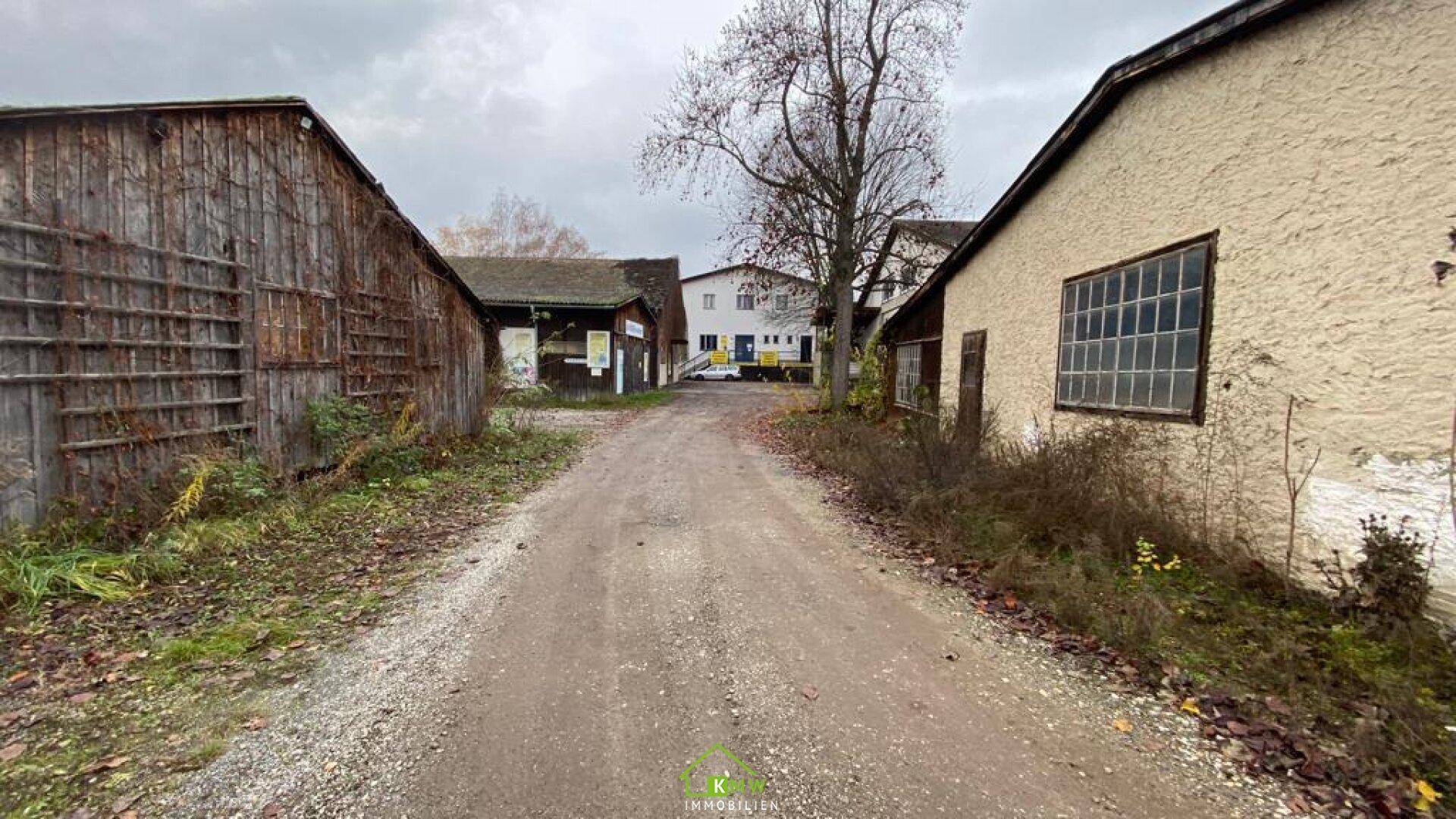 Unbefestigter Weg zwischen zwei älteren Gebäuden mit Holzfassaden und großen Fenstern, die Renovierung benötigen.