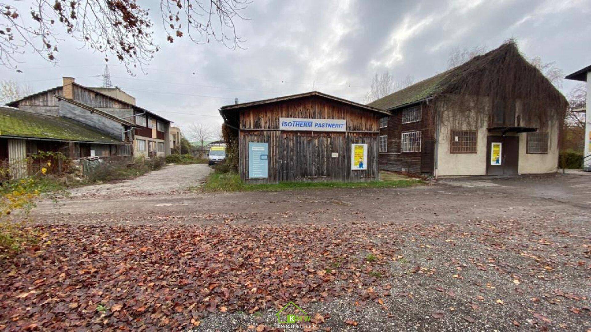 Alte Gebäude mit Holzfassaden und bewachsenen Wänden in einem ländlichen oder industriellen Umfeld, bedeckt mit Herbstlaub.