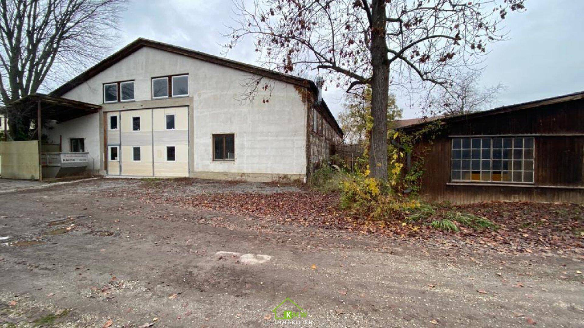 Großes, älteres Industriegebäude mit vielen Fenstern und einem kleineren Holzschuppen daneben, das Renovierung benötigt.