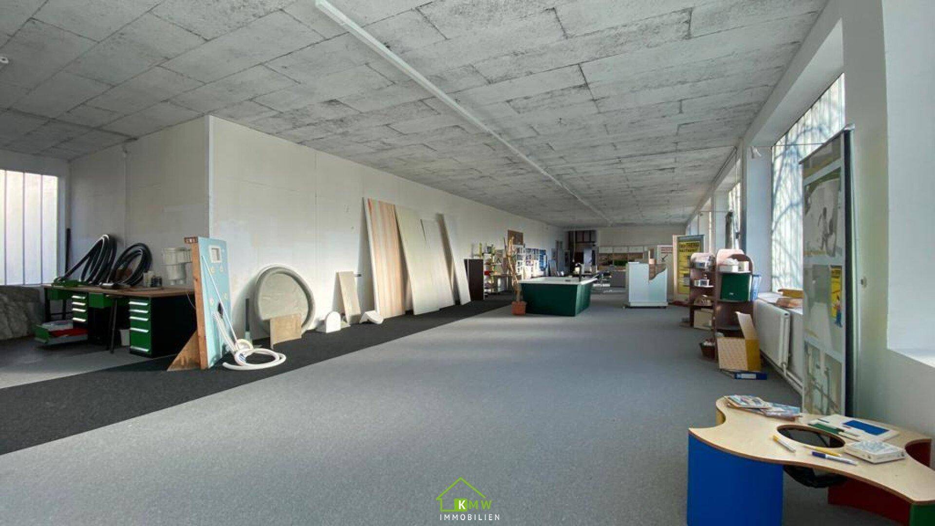 Großer, offener Raum mit Teppichboden, hohen Decken und verschiedenen Ausstellungsstücken.