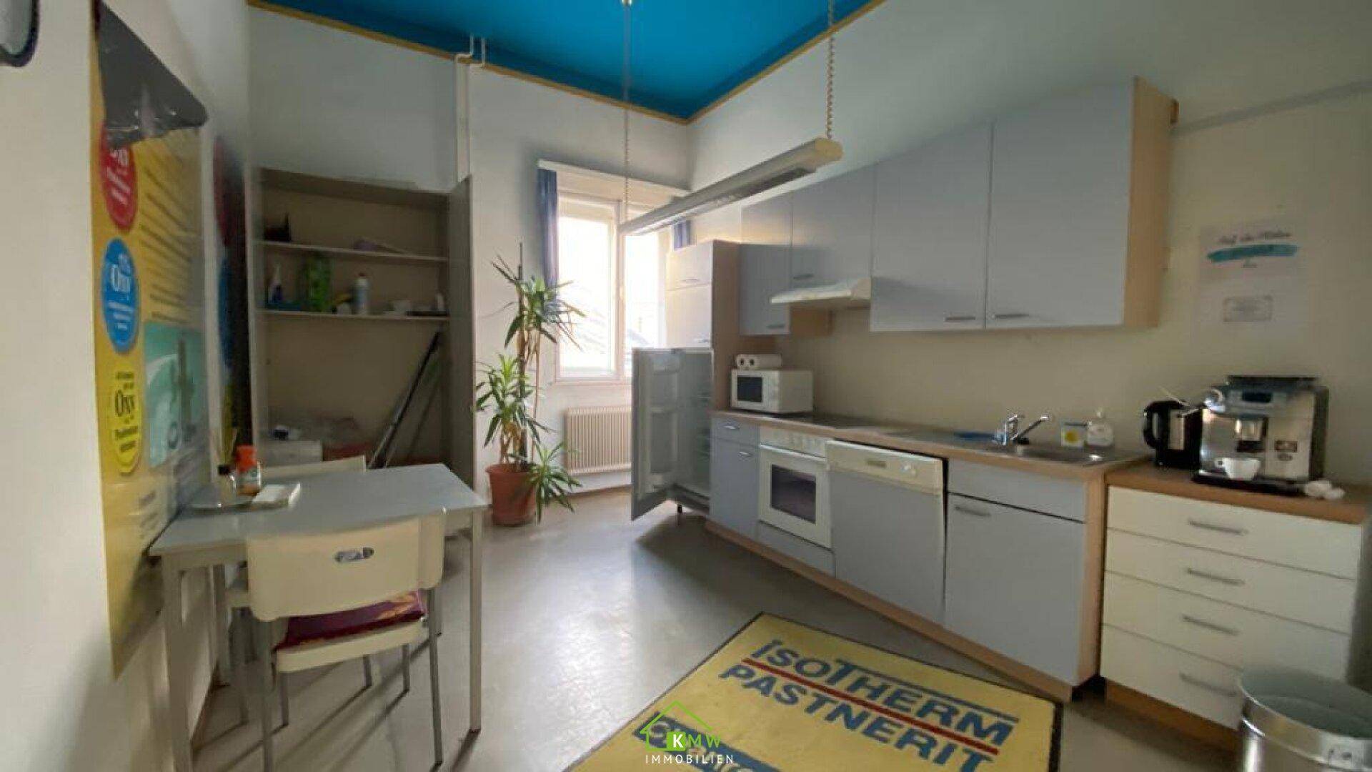 Kleine Küche oder Teeküche mit Schränken, Spüle, Kühlschrank und Mikrowelle.