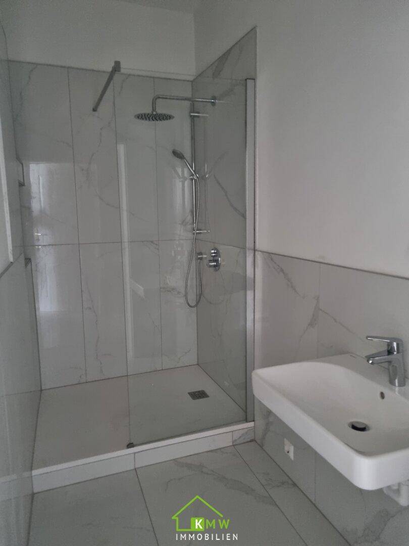 Modernes Badezimmer mit begehbarer Dusche, Marmoroptik-Fliesen und minimalistischem Waschbecken.