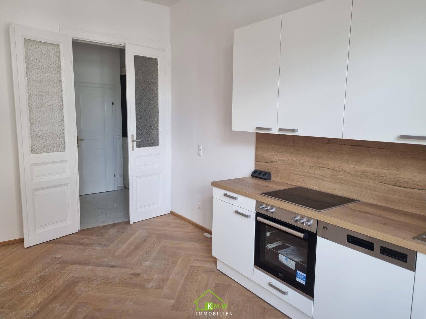 Moderne Einbauküche mit weißen Schränken, Holzarbeitsplatte und Fischgrätparkettboden.