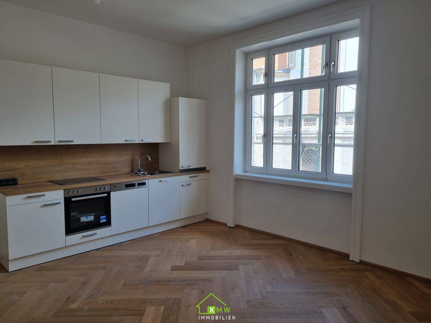 Helle Küche mit Einbaugeräten, Holzarbeitsplatte und großem Fenster für viel Tageslicht.