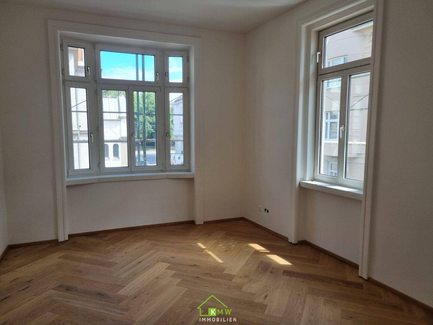 Heller, leerer Raum mit elegantem Fischgrätparkett und großen Fenstern für optimale Belichtung.