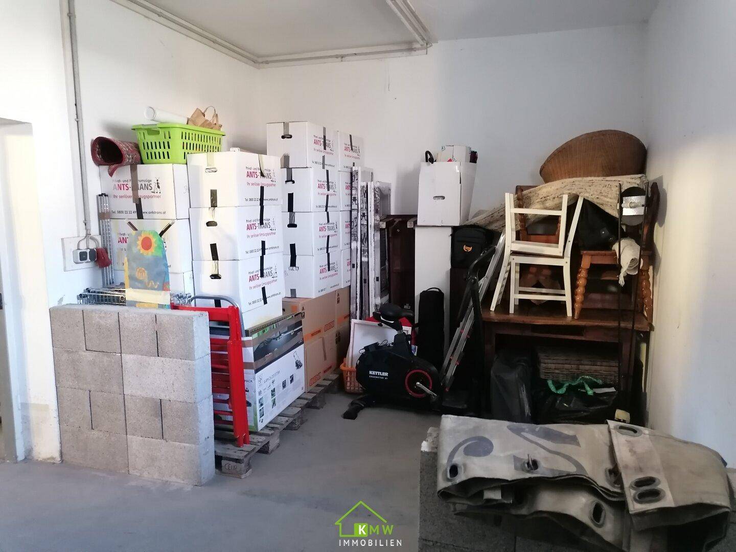 Unaufgeräumter Abstellraum oder Lagerbereich mit vielen Kartons, Baumaterialien und einem Heimtrainer.