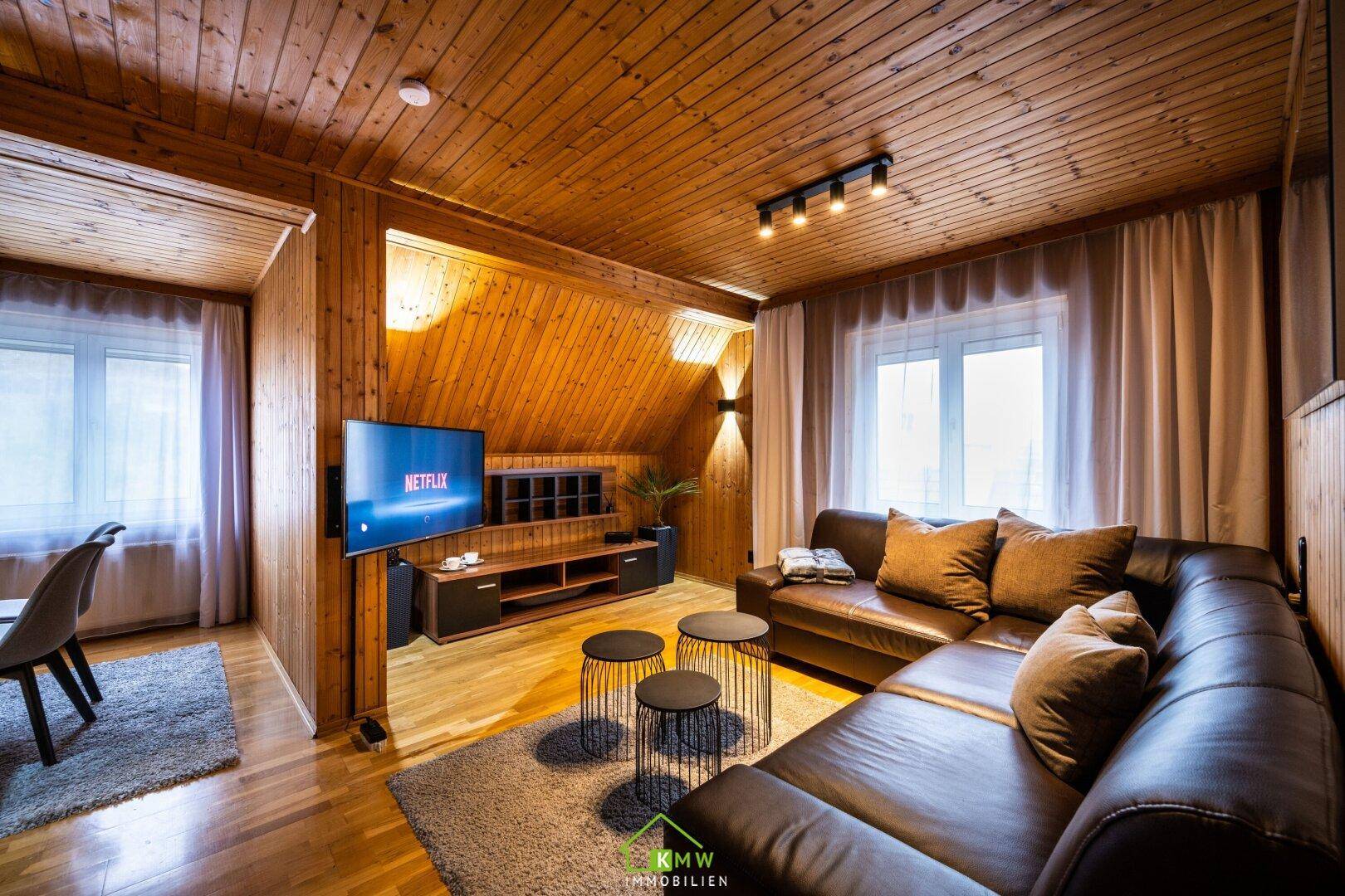 Rustikales Wohnzimmer mit Holzvertäfelung, Ledersofa und Fernseher an der Wand.