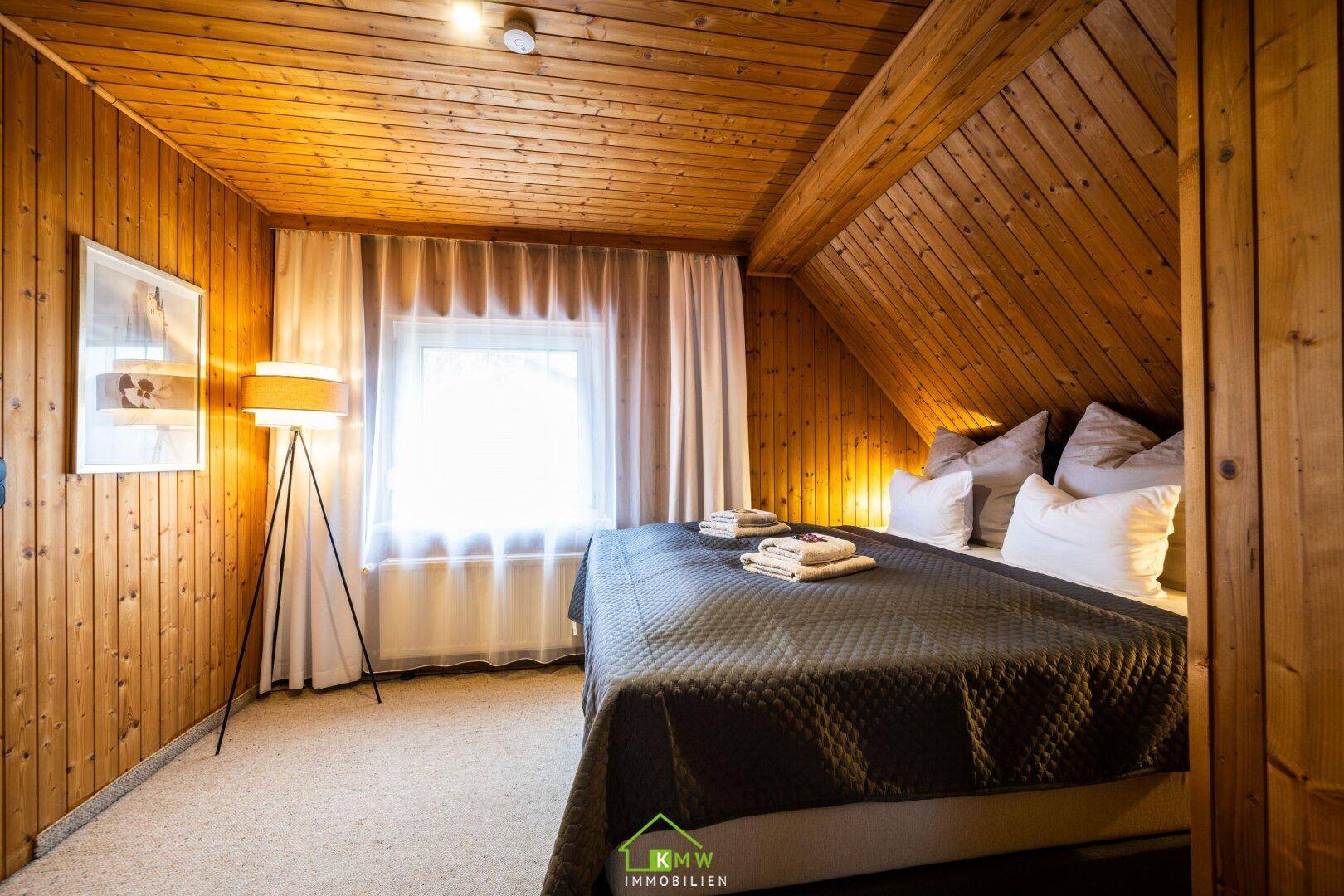 Schlafzimmer mit Holzvertäfelung, Teppichboden und einem großen Fenster mit Vorhängen.