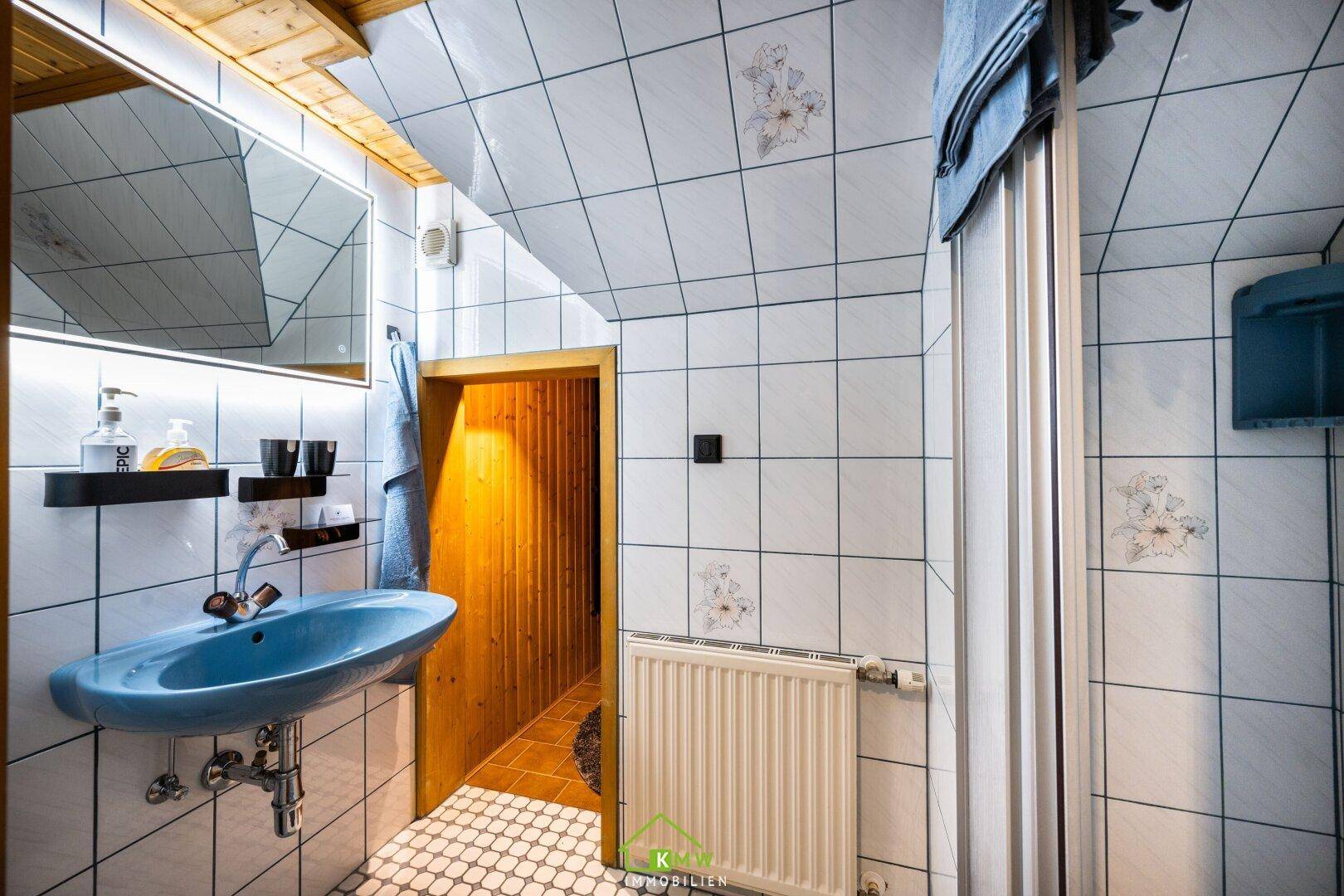 Badezimmer mit blauer Waschbecken, weißen Fliesen und Zugang zu einer Sauna.