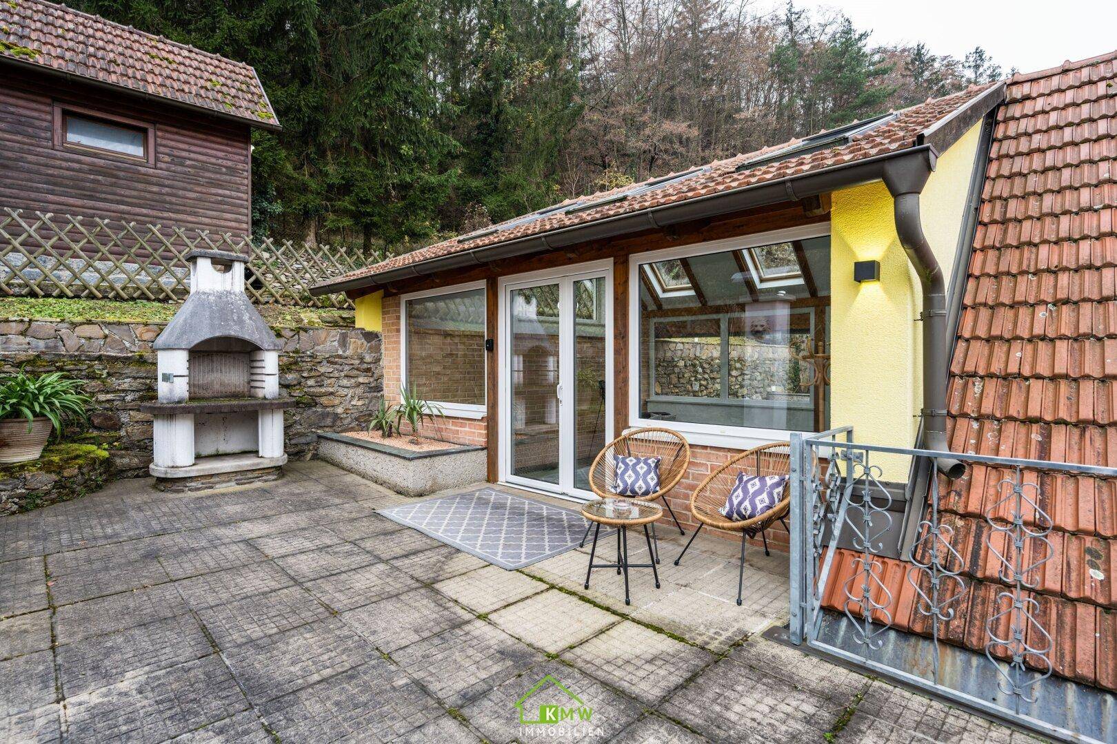 Gepflasterte Terrasse mit Grillplatz, Sitzgelegenheiten und Blick auf die Umgebung.