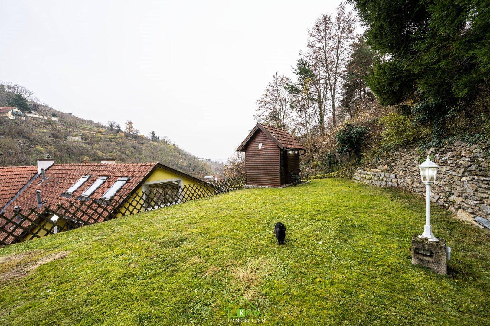 Großer, gepflegter Gartenbereich mit Rasenfläche, Gartenhaus und Blick auf die Hügellandschaft.