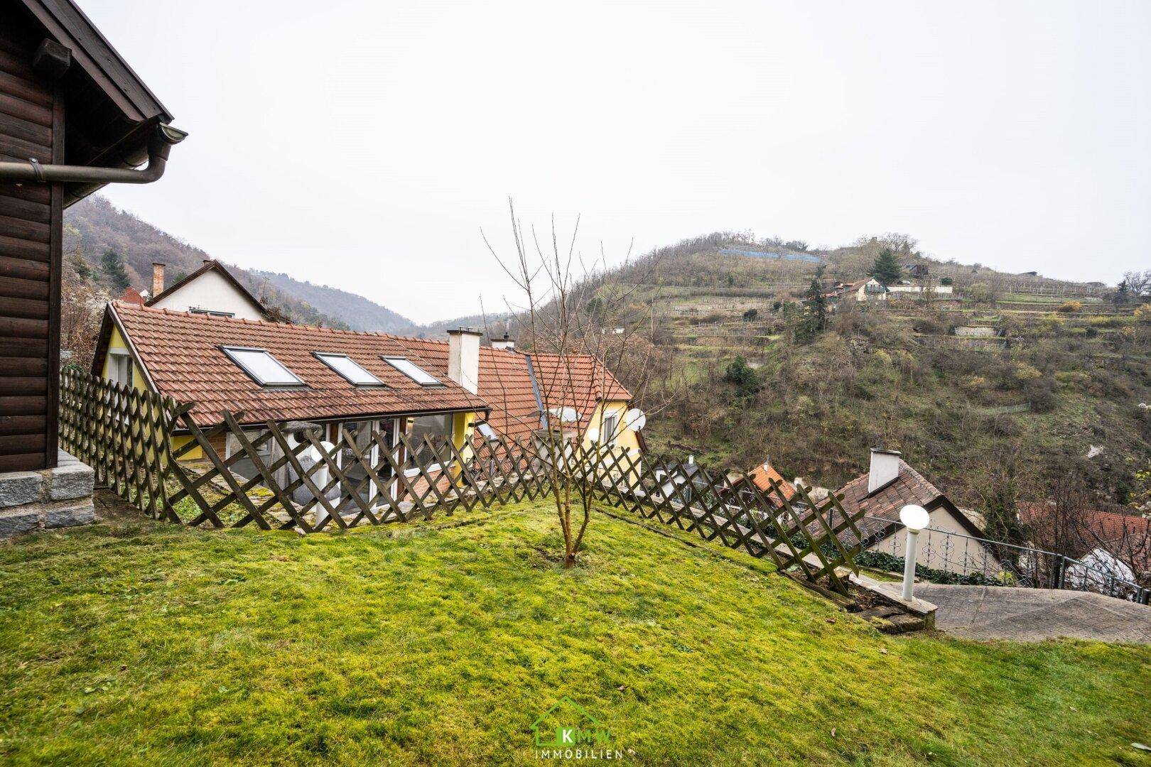 Weitläufiger Garten mit Rasen, Holzzaun und Blick auf die umliegenden Weinberge.