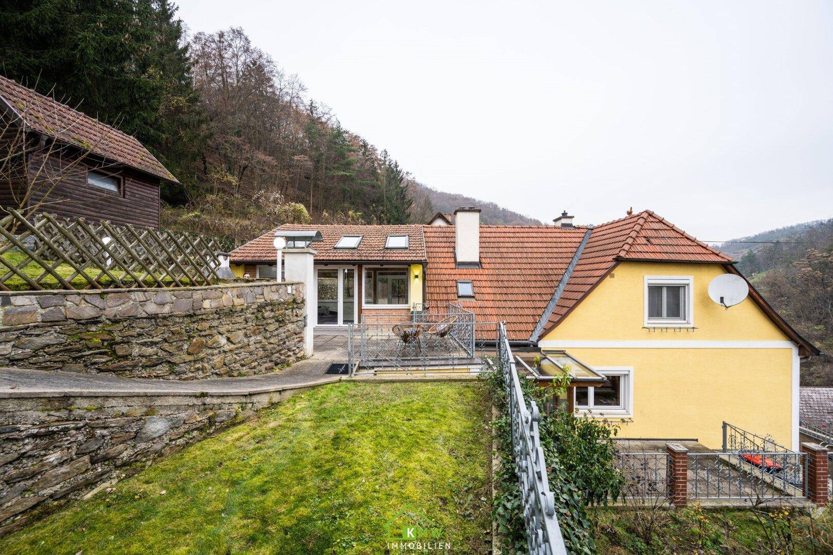 Seitenansicht des Hauses mit Terrasse, Garten und Blick auf die bewaldete Umgebung.