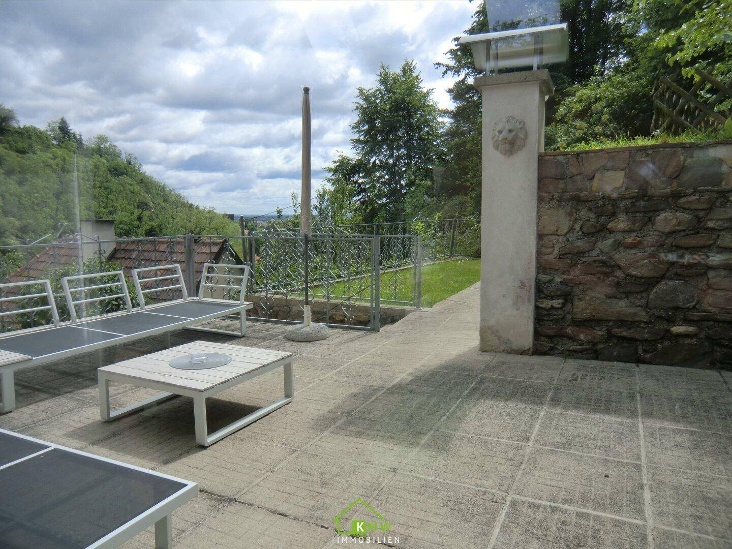 Große gepflasterte Terrasse mit Gartenmöbeln und weitem Blick über die Landschaft.