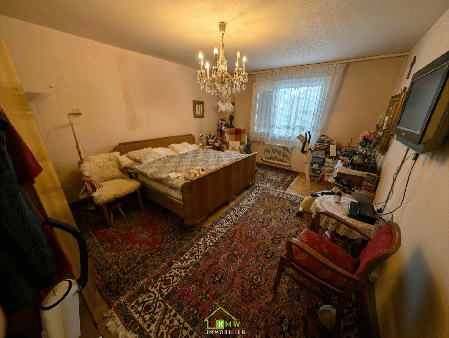 Schlafzimmer mit großem Bett, Teppichboden, Kronleuchter und traditioneller Einrichtung.