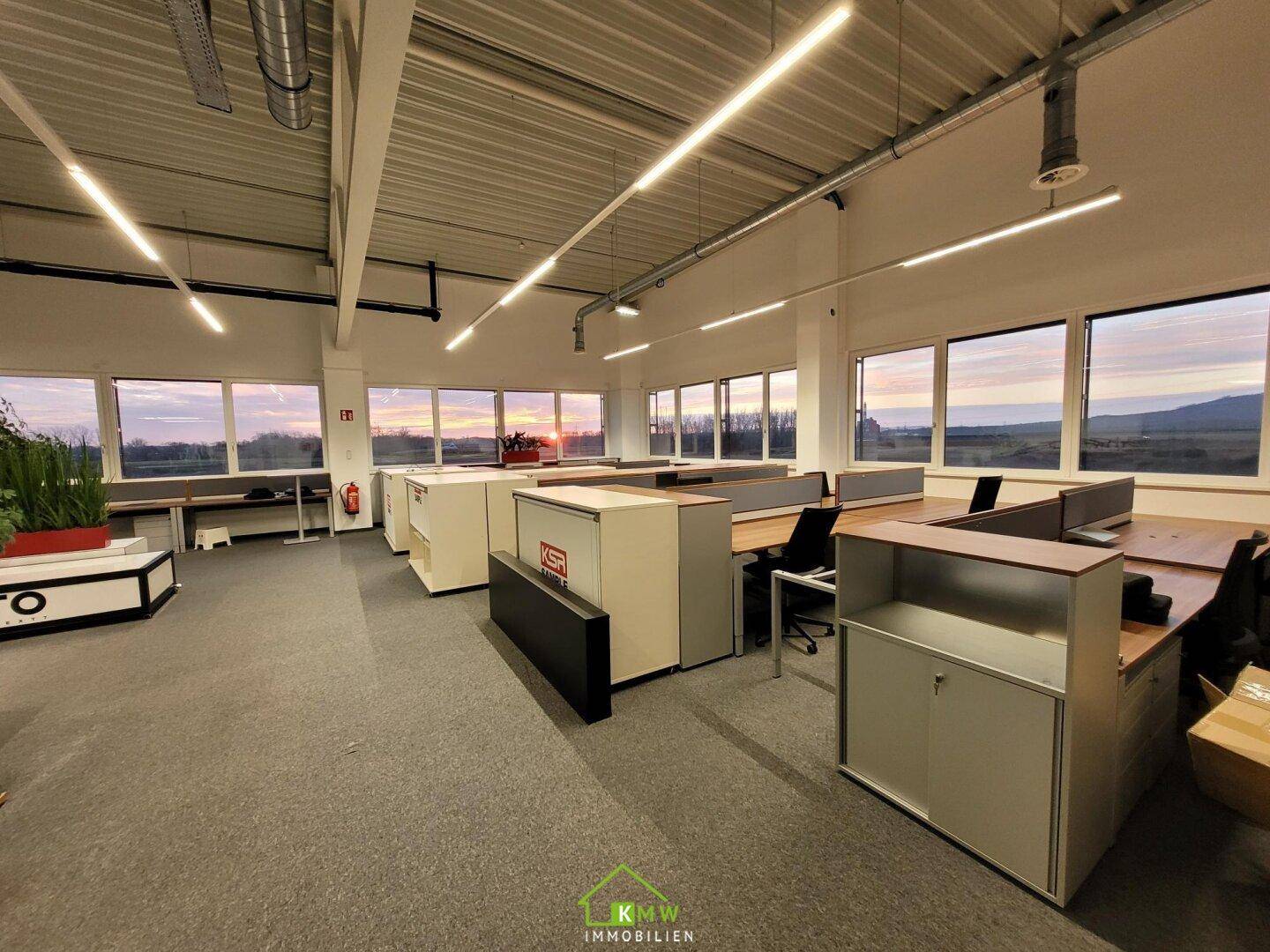 Helles Großraumbüro mit ergonomischen Arbeitsplätzen, Teppichboden und Panoramablick auf die Landschaft.