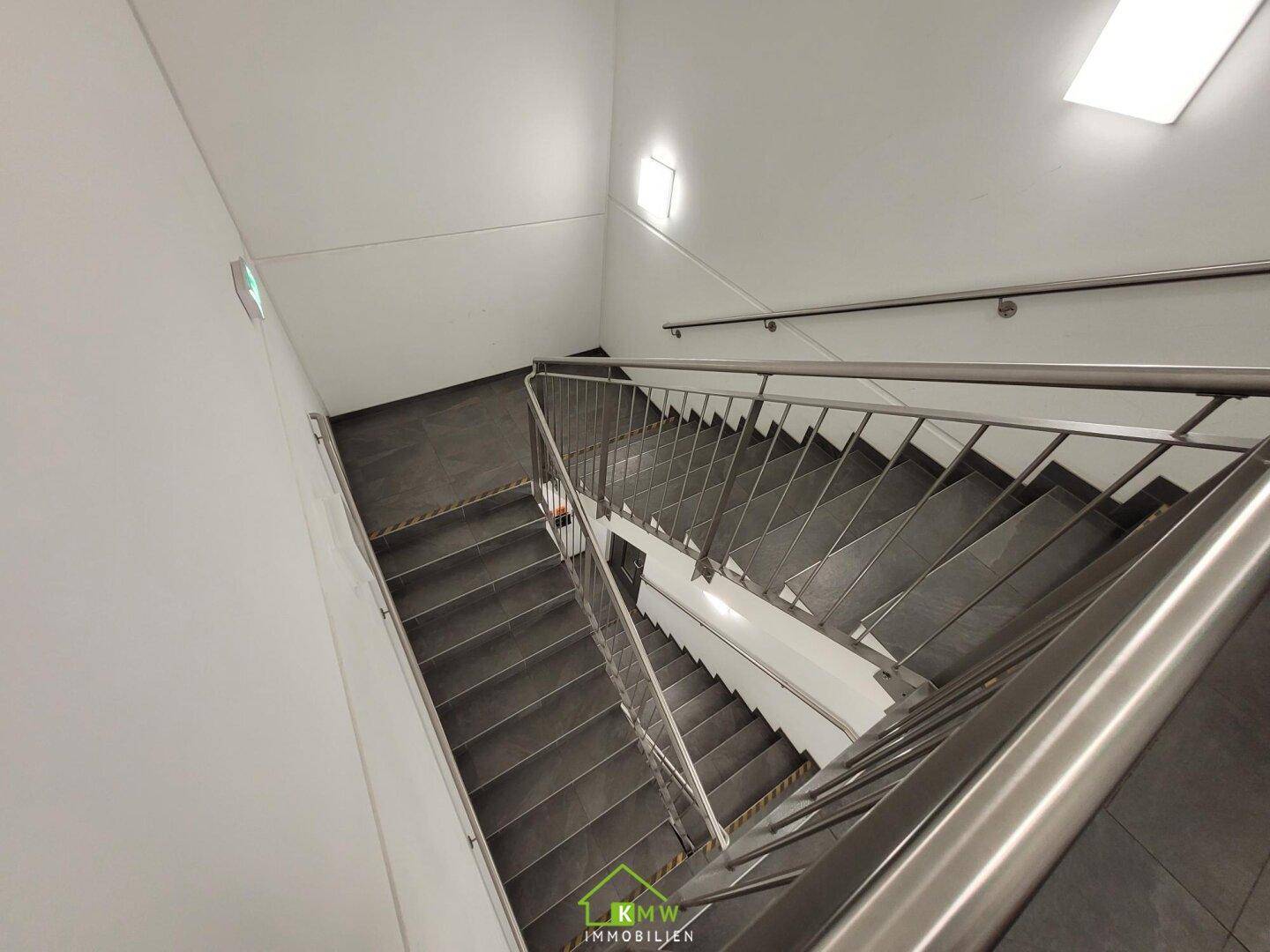 Modernes Treppenhaus mit dunklen Stufen, Edelstahlgeländer und heller Beleuchtung.