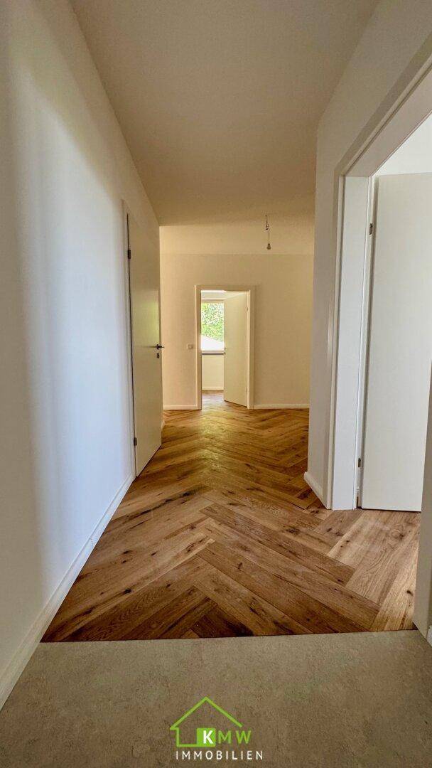 Langer Flur mit elegantem Fischgrätparkett, der zu verschiedenen Räumen führt.