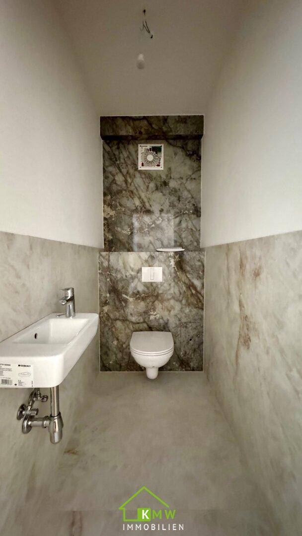Modernes Gäste-WC mit Marmorfliesen, wandhängendem WC und einem einzelnen Waschbecken.