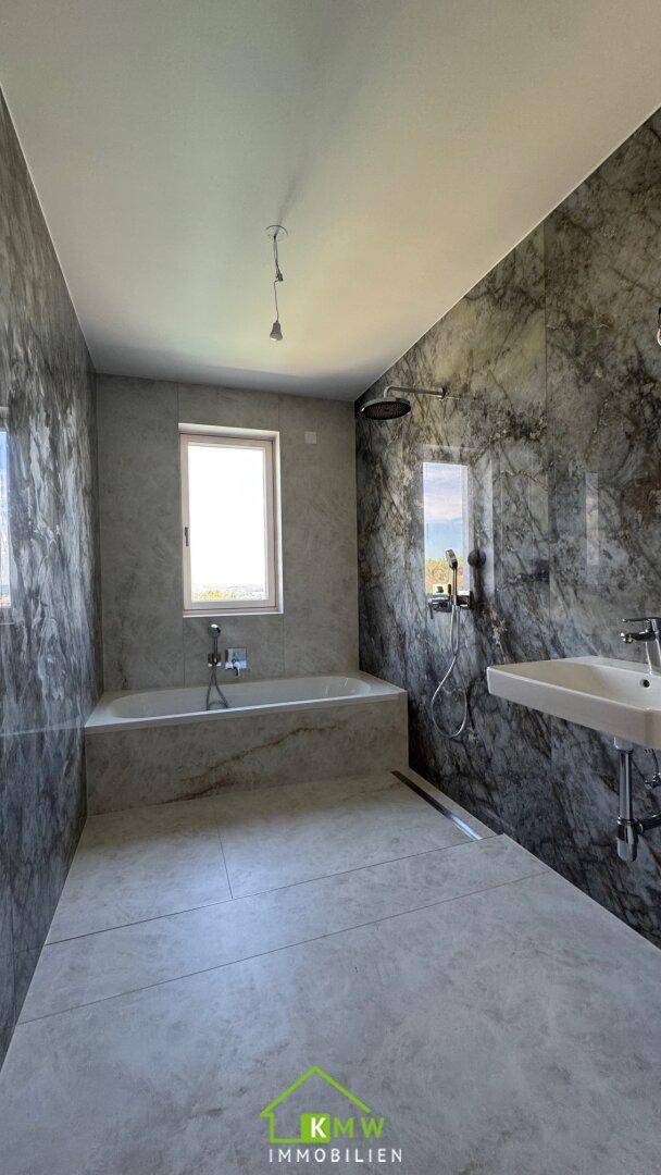 Modernes Badezimmer mit großformatigen Marmorfliesen, Badewanne, Regendusche und Fenster für natürliches Licht.