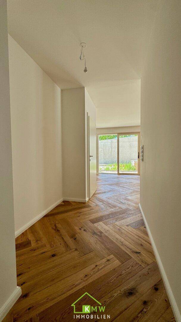 Heller Flur mit elegantem Fischgrätparkett, der zu einem Raum mit Terrassenzugang führt.