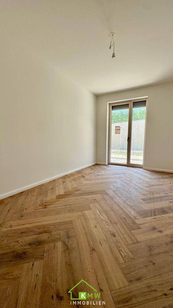 Helles Zimmer mit elegantem Fischgrätparkett und großem Glaszugang zu einem Außenbereich.