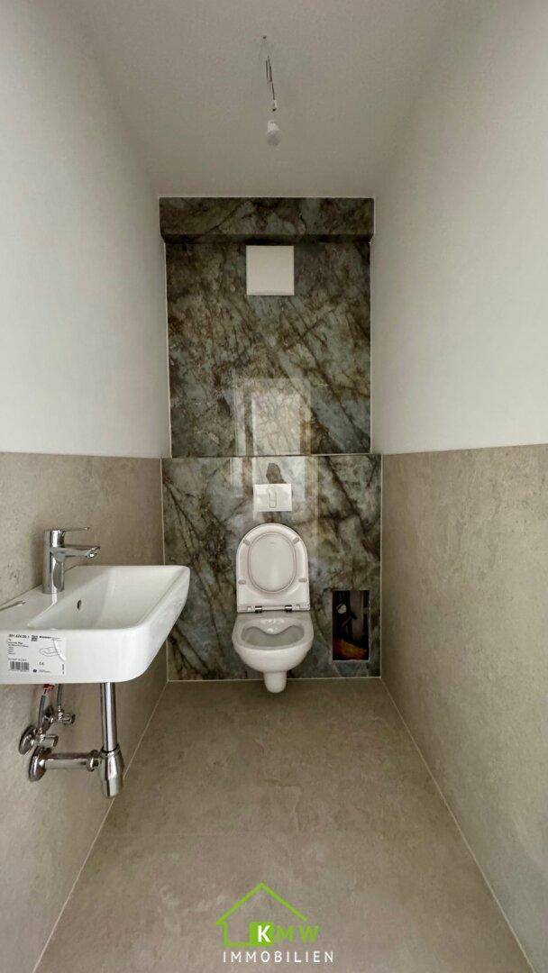 Gäste-WC mit wandhängender Toilette und modernem Waschbecken, teilweise mit Marmorfliesen.