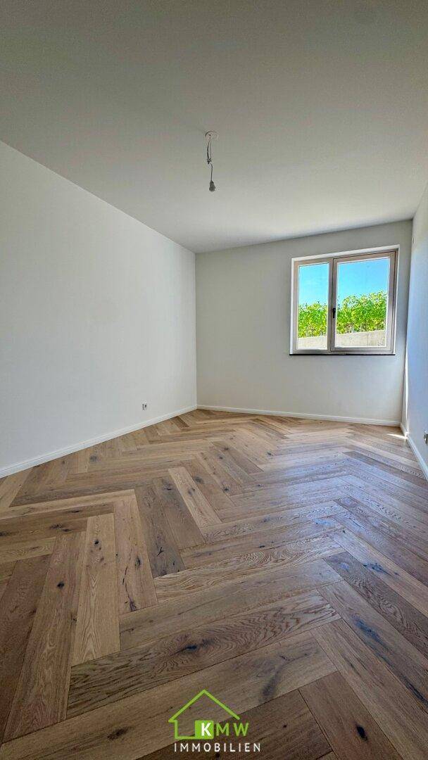 Heller Raum mit Fischgrätparkettboden und einem Fenster mit Blick ins Grüne.