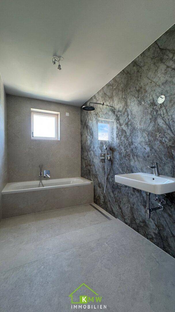 Modernes Badezimmer mit großformatigen Fliesen, Badewanne und Regendusche.