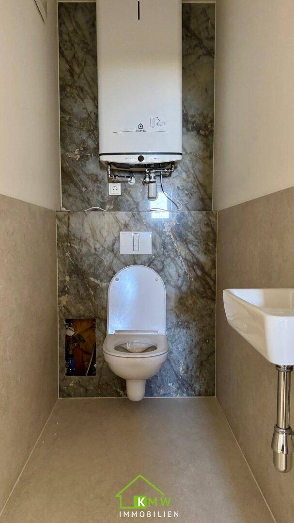 Gäste-WC mit Wand-WC, kleinem Waschbecken und modern gefliesten Wänden.
