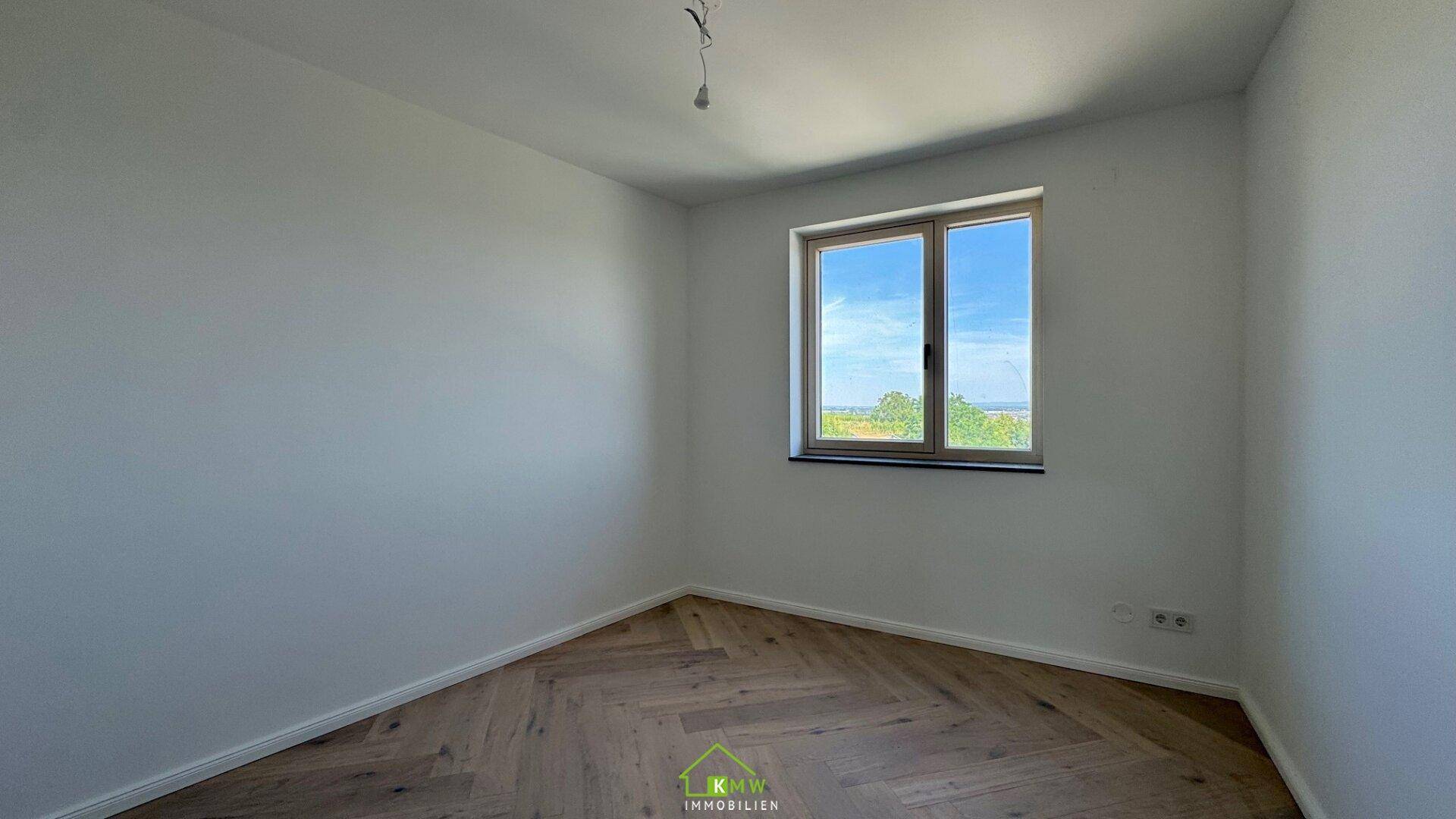 Lichtdurchflutetes Zimmer mit Fischgrätparkett und Blick ins Grüne.