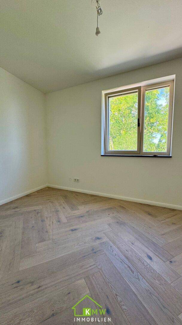 Geräumiges Zimmer mit Fischgrätparkettboden und Fenster mit Grünblick.