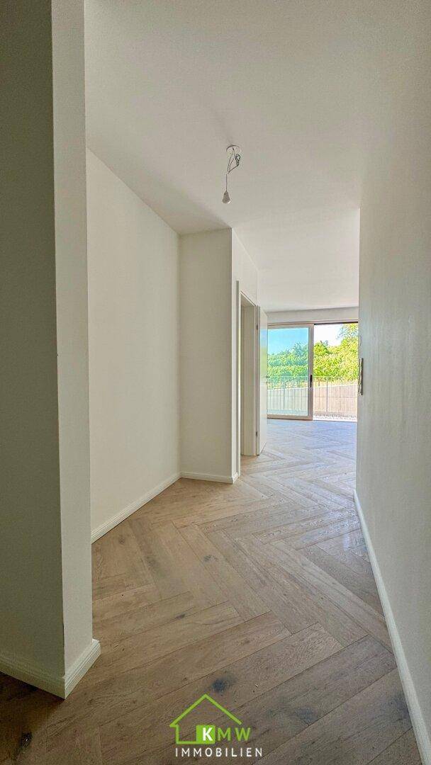 Heller Flur mit Fischgrätparkettboden und Zugang zu einem Balkon.