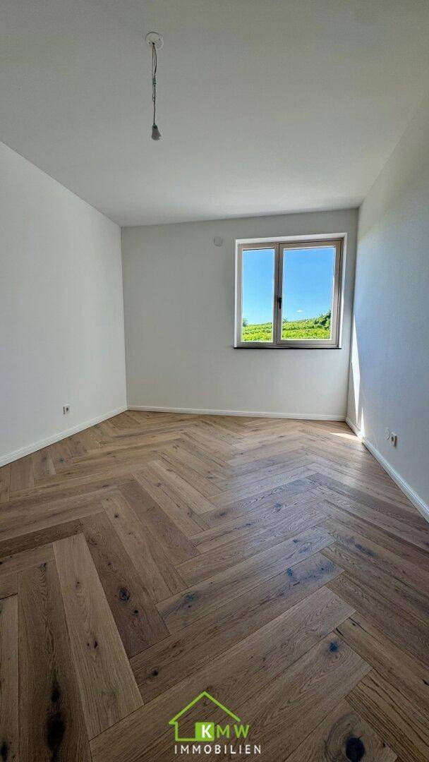 Lichtdurchflutetes Zimmer mit Fischgrätparkett und weitem Blick auf die grüne Landschaft.