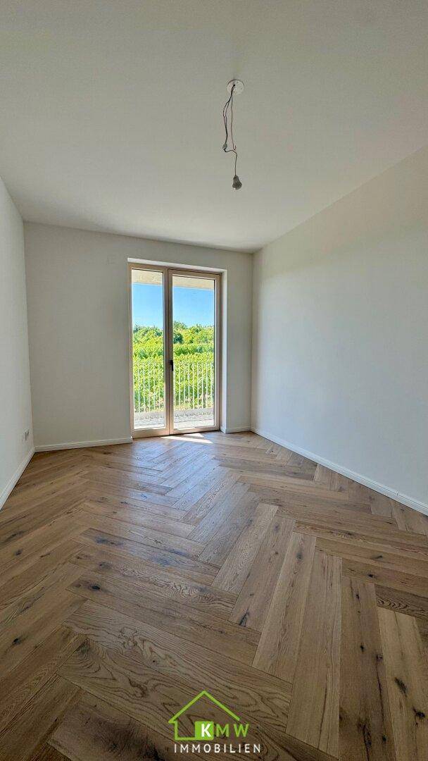 Helles Zimmer mit Fischgrätparkett und Zugang zu einem Balkon mit Blick ins Grüne.