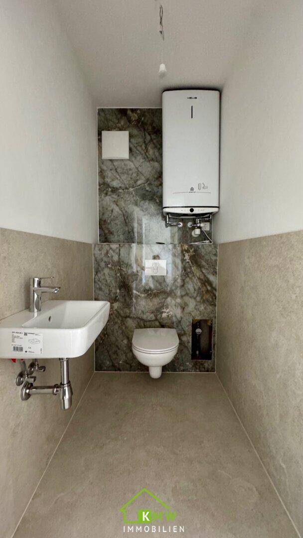 Gäste-WC mit modernem Waschbecken, Wand-WC und einer stilvollen Marmor-Akzentwand.
