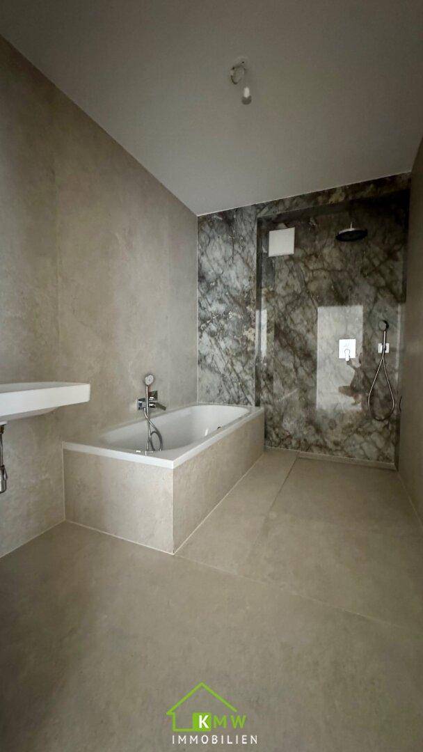 Modernes Badezimmer mit Badewanne, begehbarer Dusche und eleganten Marmorfliesen an den Wänden.