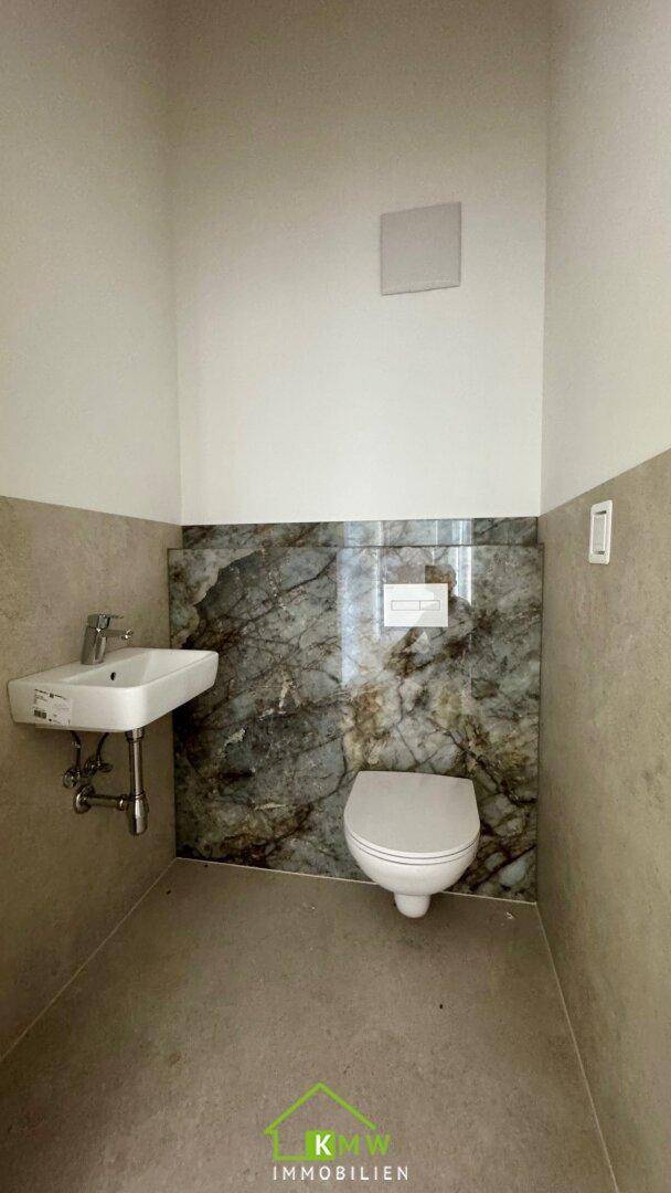 Modernes Gäste-WC mit Wand-WC, Einzelwaschbecken und stilvoller Marmor-Akzentwand.