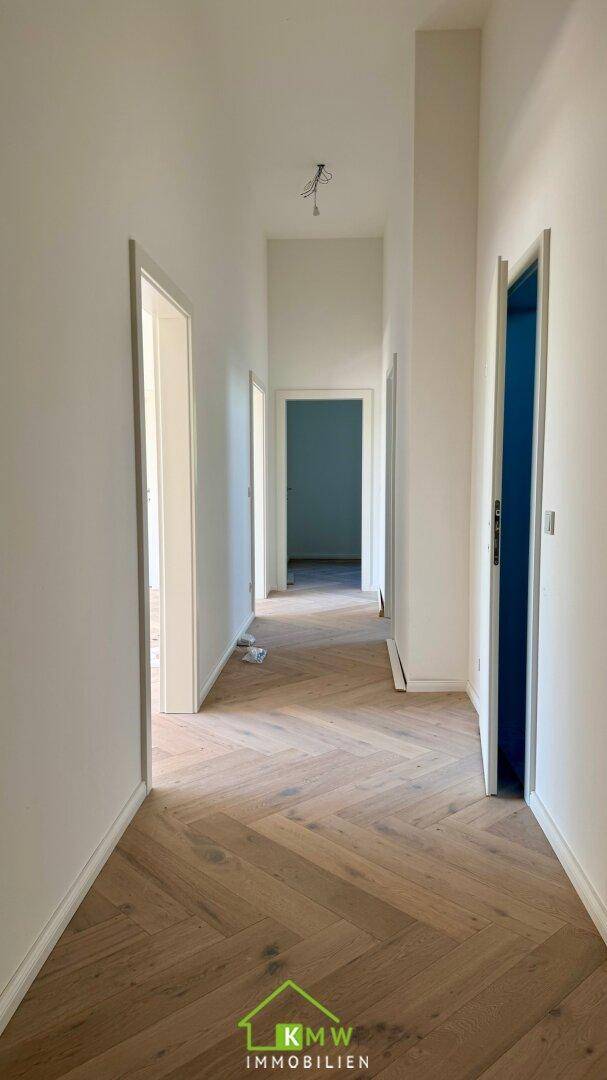 Heller Flur mit elegantem Fischgrätparkett und weißen Wänden in einem Neubau.