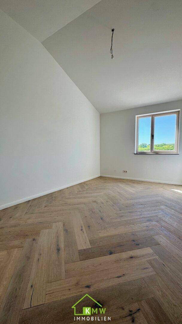 Geräumiges Zimmer mit Fischgrätparkett, weißen Wänden und einem Fenster mit Ausblick.