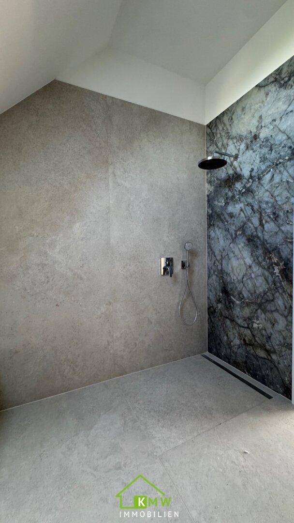 Geräumige Dusche mit modernen grauen Fliesen und einer eleganten Marmor-Akzentwand.