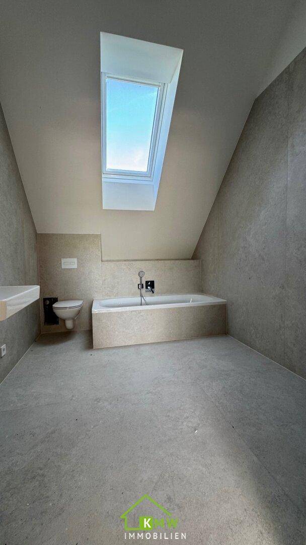 Modernes Badezimmer mit Badewanne, Wand-WC, grauen Fliesen und Dachfenster.